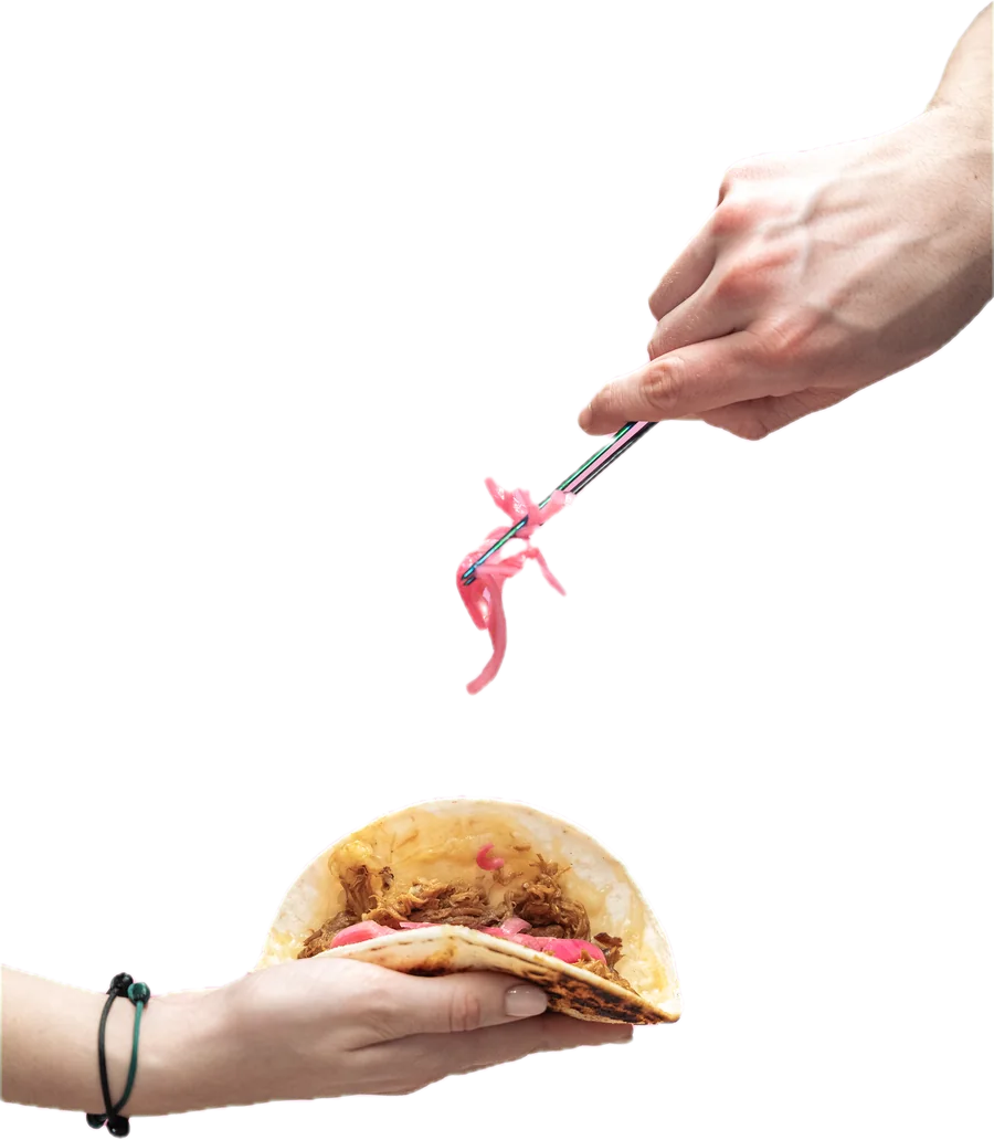 Tweezers placing pickled onion onto a taco held in a hand